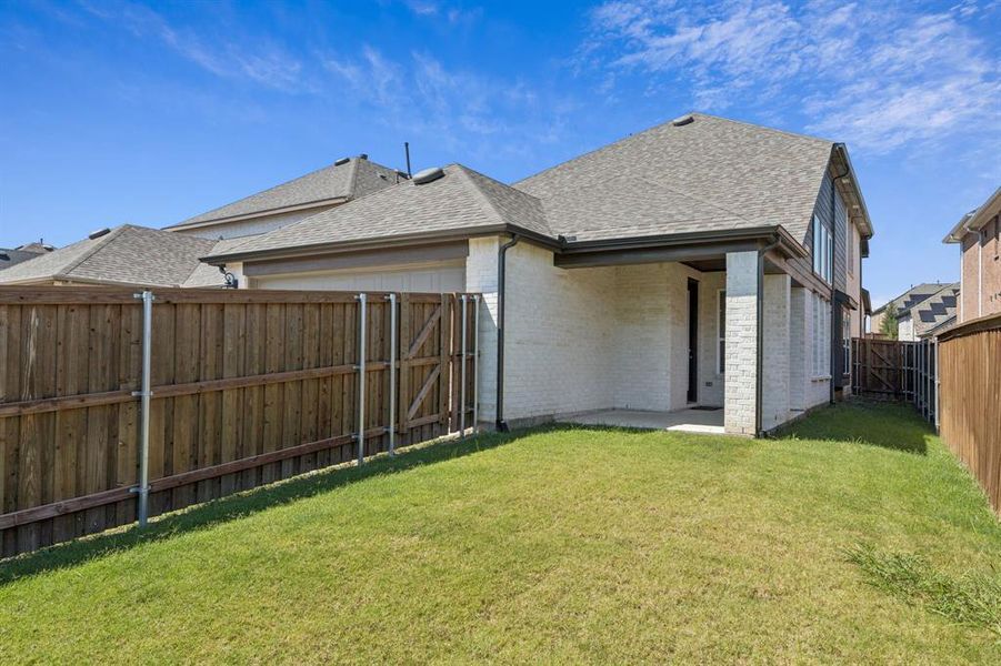 Back of house with a shingled roof, a patio, brick siding, a fenced backyard, and a gate Back of house with a shingled roof, a patio, brick siding, a fenced backyard, and a gate