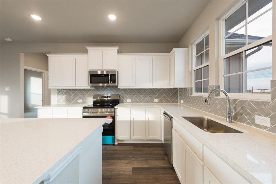 Kitchen featuring stainless steel appliances, white cabinets, light stone counters, dark wood finished floors, and recessed lighting