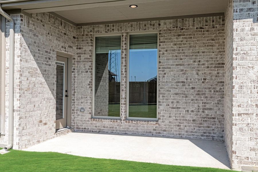 Covered back patio with concrete slab, light brick exterior, large window, and side entry door Covered back patio with concrete slab, light brick exterior, large window, and side entry door