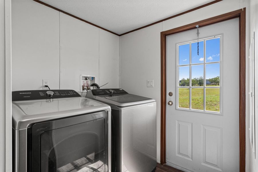 Washroom with ornamental molding, washer and clothes dryer, dark wood-type flooring, and a textured ceiling