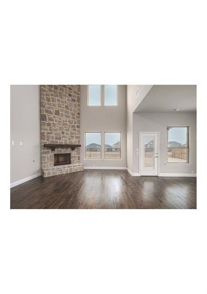 Unfurnished living room featuring a stone fireplace, dark hardwood / wood-style flooring, and a high ceiling