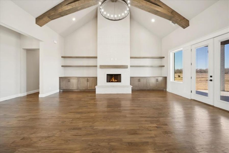 Unfurnished living room with dark hardwood / wood-style floors, a fireplace, beamed ceiling, an inviting chandelier, and french doors