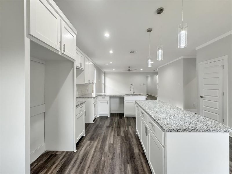 Kitchen with white cabinets, a center island, dark wood finished floors, crown molding, and light stone countertops Kitchen with white cabinets, a center island, dark wood finished floors, crown molding, and light stone countertops