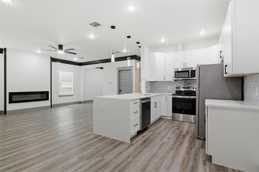 Open-concept living space featuring wood-finish flooring, a contemporary fireplace, and a ceiling fan
