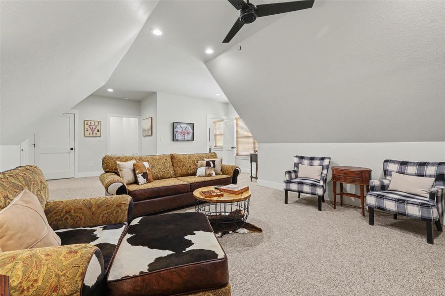 Game room above garage,  light colored carpet, vaulted ceiling, and ceiling fan