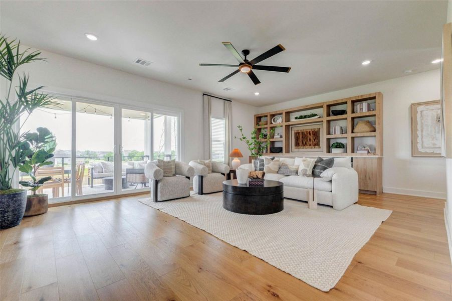 The spacious living room showcases an open-concept design ideal for both relaxing and entertaining. A modern ceiling fan, expansive windows, and sliding glass doors fill the space with natural light. The layout easily accommodates multiple seating areas, while the clean lines and neutral palette create a calm and inviting atmosphere throughout the home. The picture shown is from the model home with the same floor plan, Rev floor plan.