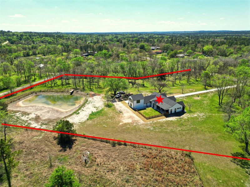 Aerial view of a spacious property with a modern house, a pond, and surrounding greenery. The boundaries are marked in red, showcasing ample land for privacy and outdoor activities.
