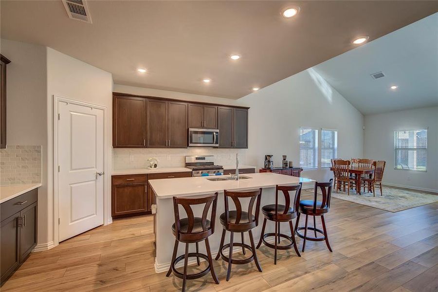 Kitchen with light wood-type flooring, a kitchen island with sink, appliances with stainless steel finishes, and tasteful backsplash