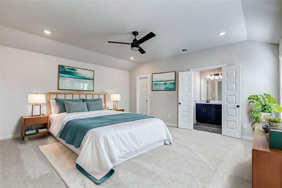 A spacious retreat with neutral tones, plush carpeting, and recessed lighting. The primary bedroom's highlight is its direct access to an ensuite bathroom through elegant double doors.