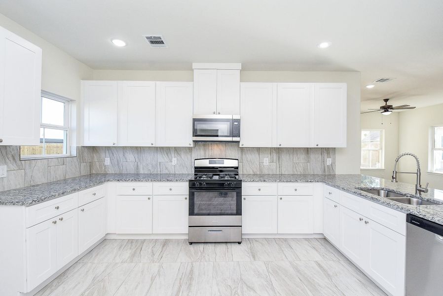 Modern kitchen with white cabinetry, stainless steel appliances, marble countertops, and a tiled backsplash.