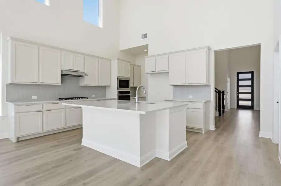 Kitchen featuring tasteful backsplash, a kitchen island with sink, white cabinets, light wood finished floors, and a towering ceiling