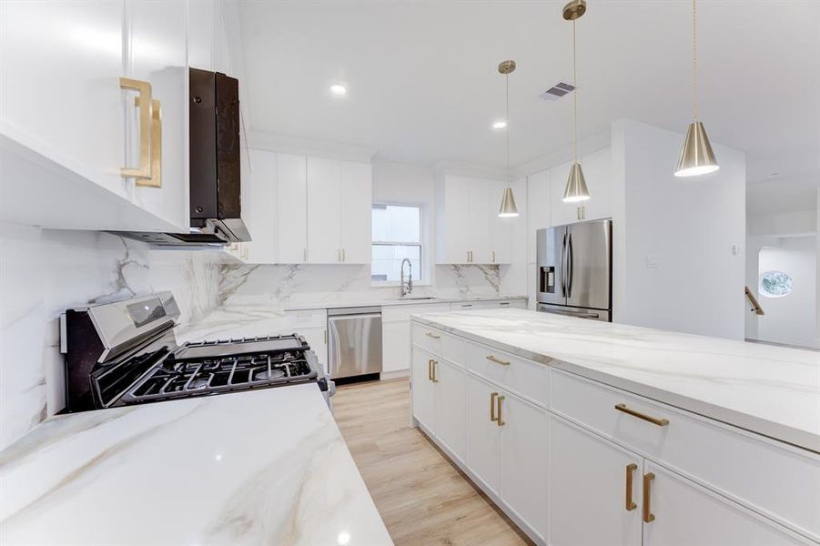 This stunning kitchen features gold hardware, quartz countertops, gas range, and stainless steel appliances. There is plenty of storage space in the cabinets.