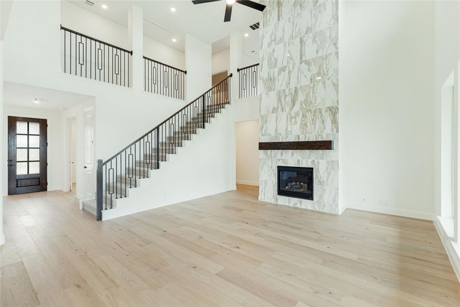 Open living area with two-story ceiling, marble fireplace, iron staircase railing, and light hardwood floors