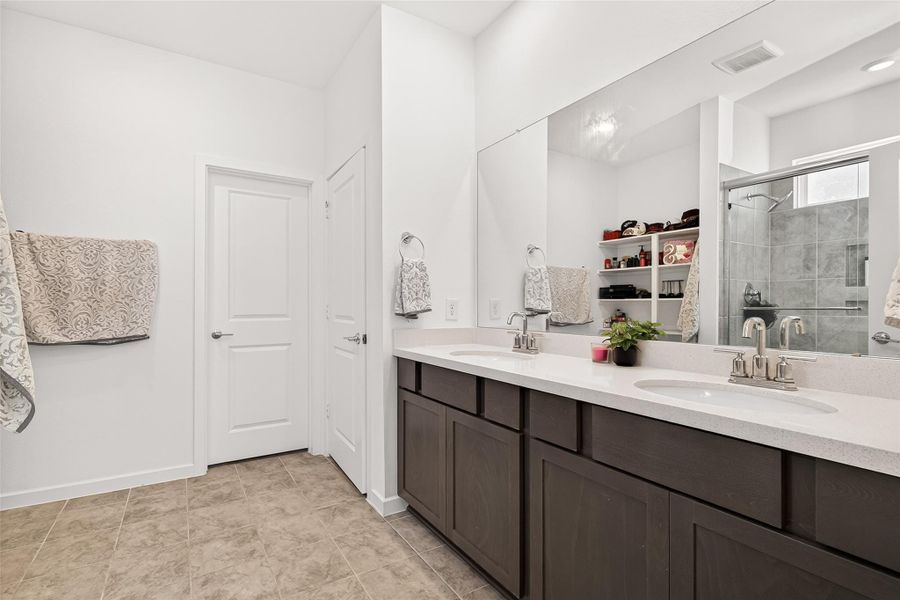 Primary bathroom featuring a spacious walk-in shower with tile surround, built-in shower niche, and natural light. Direct access to the primary closet for added convenience and functionality. Clean, bright layout with additional built-in storage shelving.