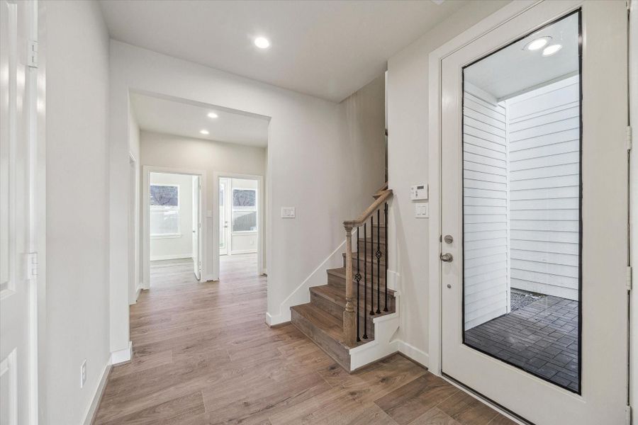 The bright, open foyer welcomes you with warm wood-toned flooring and a sophisticated staircase featuring elegant wrought-iron balusters, creating an immediate sense of home.
