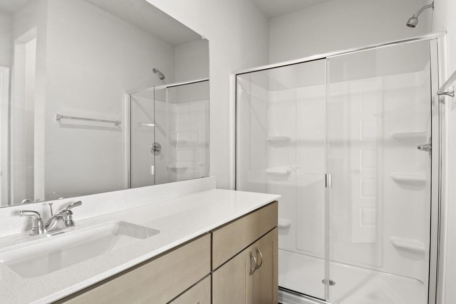 Image of primary bathroom with brown cabinets and a mirror with a white top vanity and a walk in shower