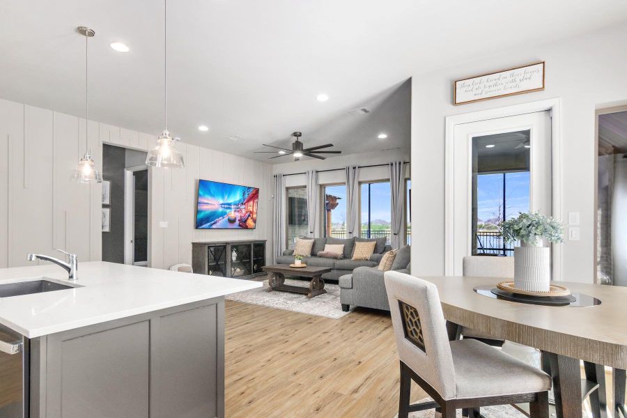 This photo showcases a modern, open-concept living area with a sleek kitchen island and pendant lighting. The cozy living space features a ceiling fan, large TV, and ample natural light from large windows and glass doors leading to a patio. The decor is contemporary, with neutral tones and stylish furnishings.