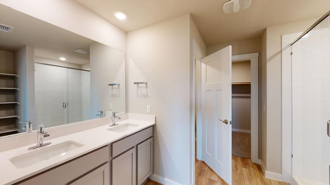 Bathroom featuring a shower stall, double vanity, a walk in closet, light wood-type flooring, and recessed lighting