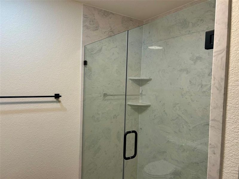 Full bathroom featuring a textured wall and a stall shower