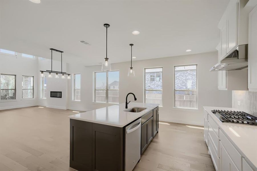 Open-concept living area featuring a kitchen island with sink, gas range, stainless steel appliances, and a fireplace
