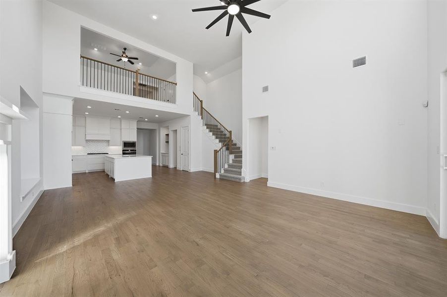 Unfurnished living room with a towering ceiling, ceiling fan, recessed lighting, dark wood-style flooring, and stairway Unfurnished living room with a towering ceiling, ceiling fan, recessed lighting, dark wood-style flooring, and stairway
