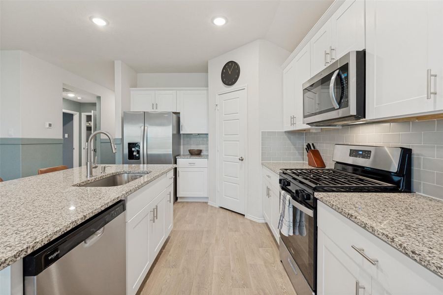 A well-appointed kitchen features stainless steel appliances, granite countertops, and light wood-look flooring.