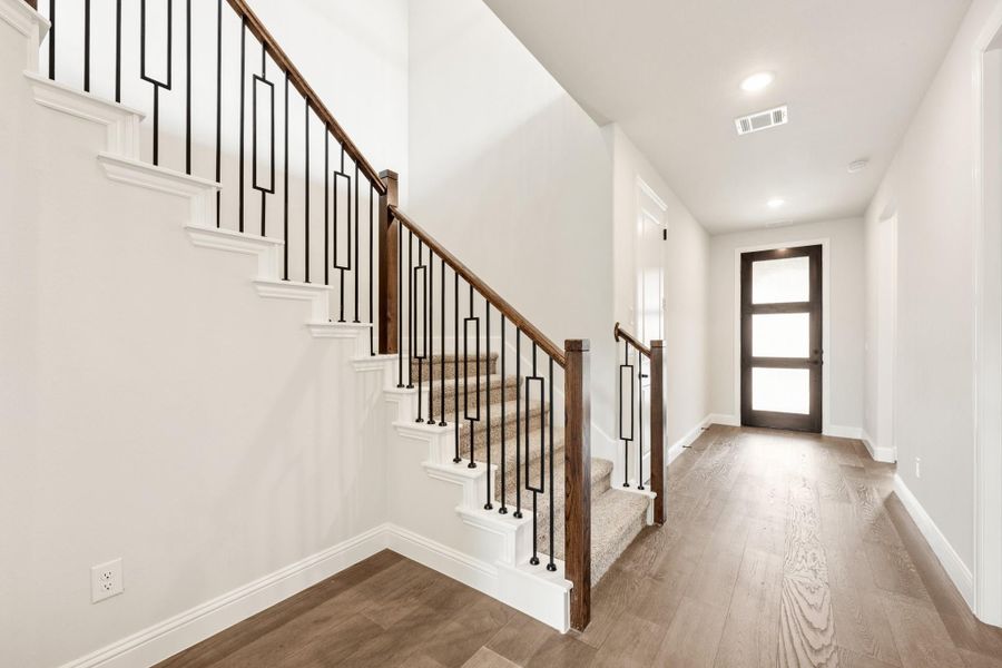 Entryway with carpeted staircase, wood and iron railing, hardwood floors, and dark wood front door with glass panels Entryway with carpeted staircase, wood and iron railing, hardwood floors, and dark wood front door with glass panels