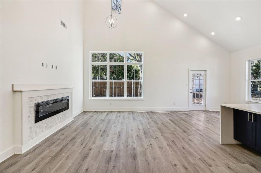Unfurnished living room featuring high vaulted ceiling, plenty of natural light, a tile fireplace, recessed lighting, and light wood-style floors Unfurnished living room featuring high vaulted ceiling, plenty of natural light, a tile fireplace, recessed lighting, and light wood-style floors