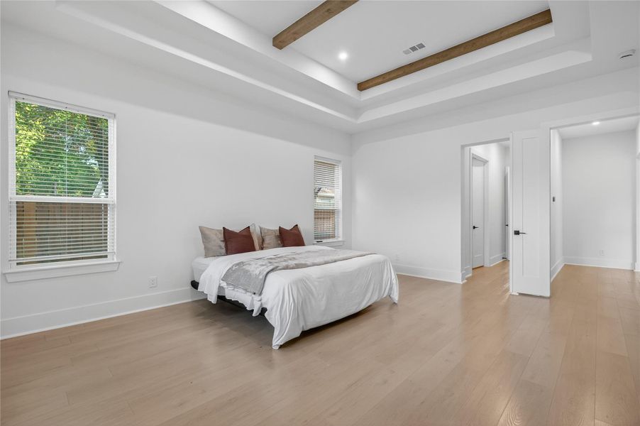Spacious primary bedroom features a decorative tray ceiling, recessed lighting, warm flooring, and multiple windows. **Images are from a previously completed project. **