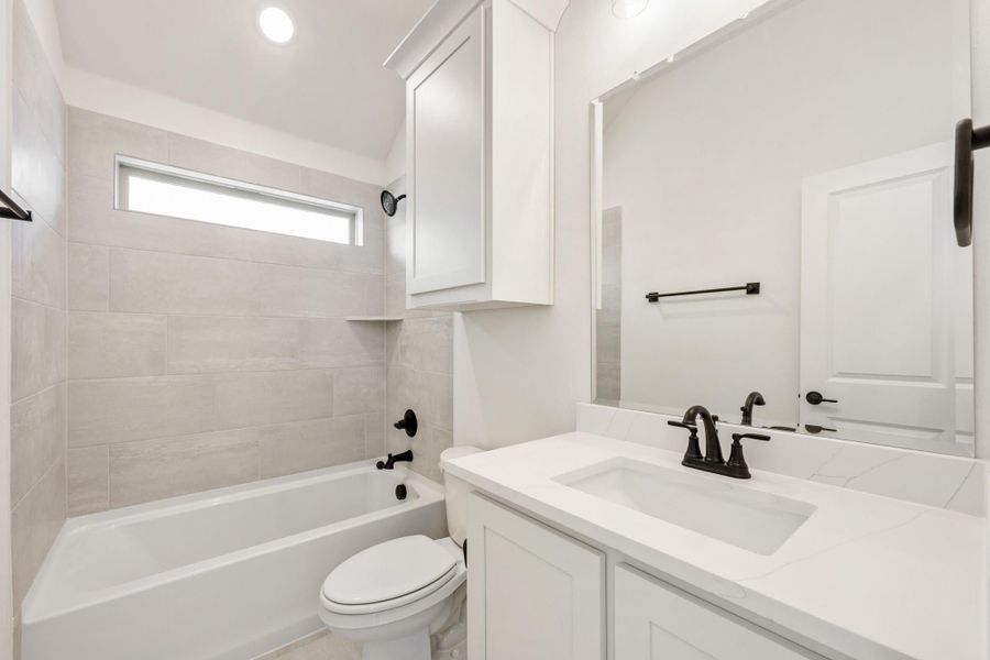 Bathroom with white vanity, tiled tub-shower combo, toilet, and black fixtures Bathroom with white vanity, tiled tub-shower combo, toilet, and black fixtures