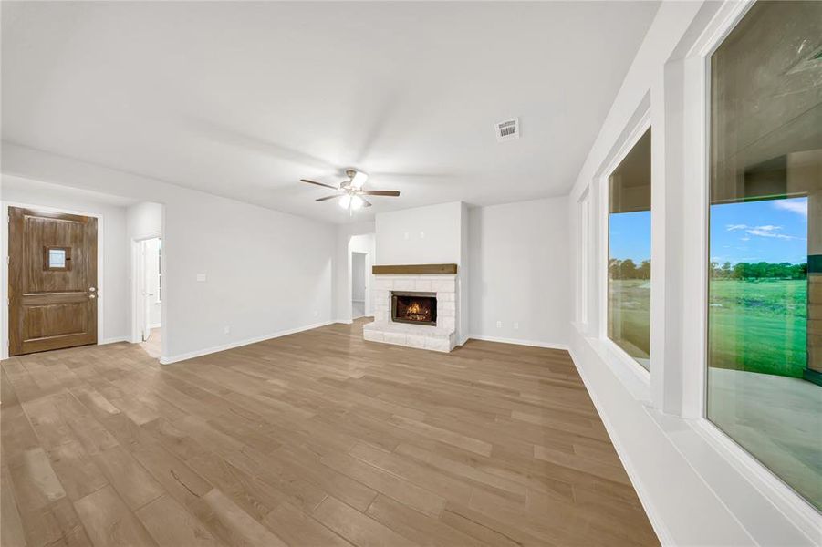 Unfurnished living room featuring ceiling fan, light wood-type flooring, and a stone fireplace Unfurnished living room featuring ceiling fan, light wood-type flooring, and a stone fireplace