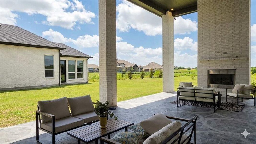 Expansive covered patio featuring a full-height brick fireplace, stamped concrete flooring, and substantial support columns