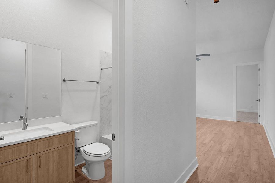 A well-appointed bathroom features a modern vanity and commode, with continuous wood flooring flowing into adjacent living spaces.