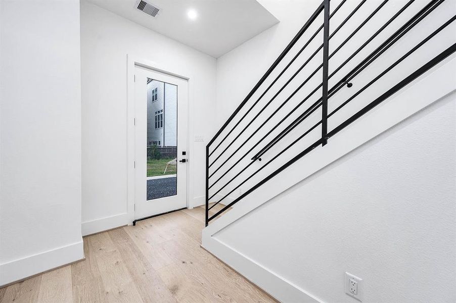 Bright entryway with modern horizontal stair railing, light hardwood floors, and a view to the outdoors through a glass-panel door. Clean and contemporary design.