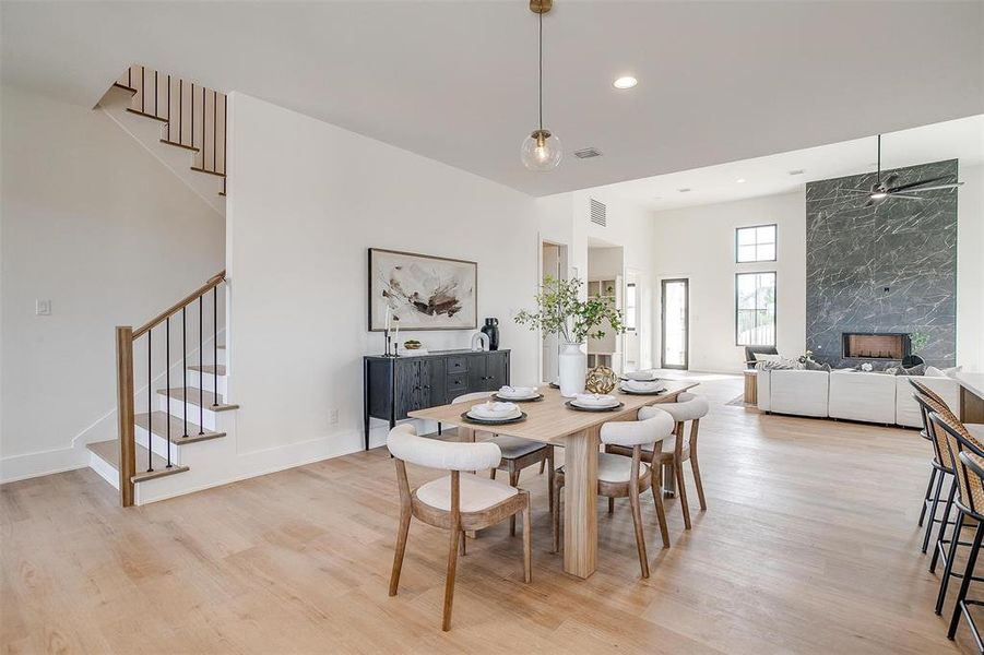 Dining space with stairs, light wood-type flooring, a high end fireplace, recessed lighting, and a high ceiling