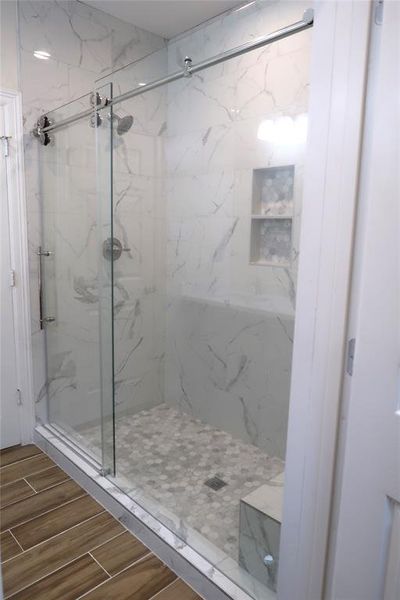 Oversized walk in ensuite shower with custom glass sliding door, a soap basin, and bench.