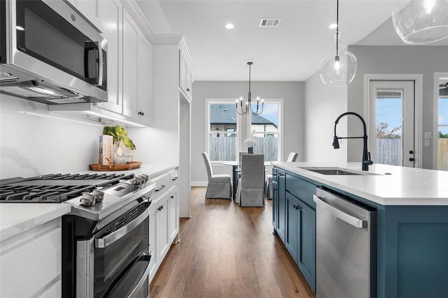 Kitchen featuring white cabinetry, appliances with stainless steel finishes, a chandelier, hanging light fixtures, and dark wood-style flooring Kitchen featuring white cabinetry, appliances with stainless steel finishes, a chandelier, hanging light fixtures, and dark wood-style flooring
