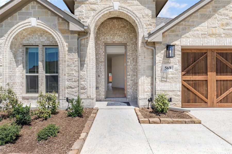 Stone home exterior with arched front entry, open door, and wood garage door beside landscaped walkway