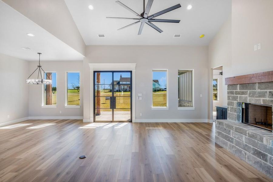 Unfurnished living room featuring a stone fireplace, high vaulted ceiling, ceiling fan with notable chandelier, and light wood-type flooring