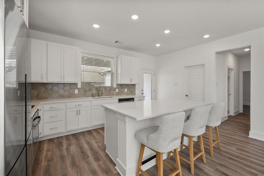 Kitchen featuring freestanding refrigerator, recessed lighting, decorative backsplash, a center island, and a breakfast bar.