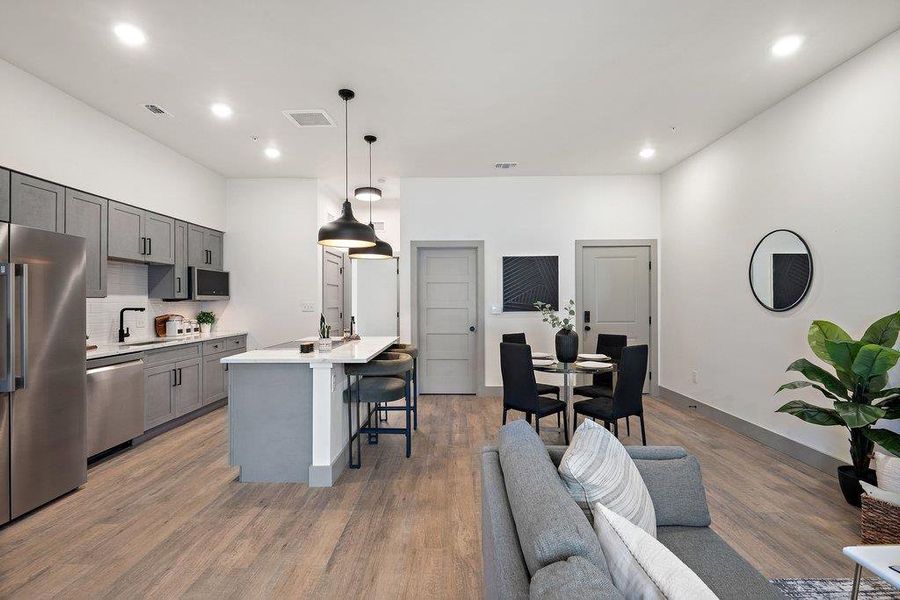 Kitchen featuring stainless steel appliances, a breakfast bar, gray cabinets, pendant lighting, and an island with sink