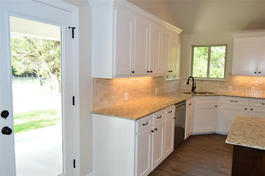 Kitchen featuring dishwasher, white cabinetry, backsplash, and vaulted ceiling