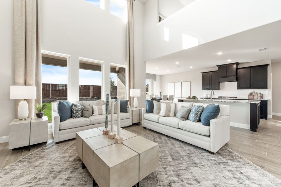 Open-concept living room with two-story ceilings, white sofas, and kitchen visible in background Open-concept living room with two-story ceilings, white sofas, and kitchen visible in background