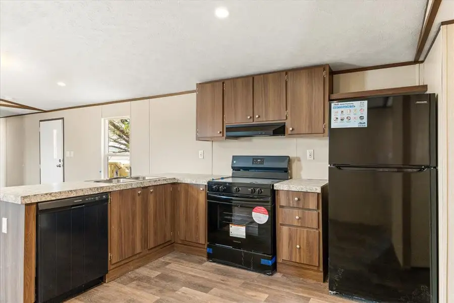 Kitchen featuring wood-finish cabinetry, light-toned countertops, a stainless steel sink, black appliances, and wood-finish flooring