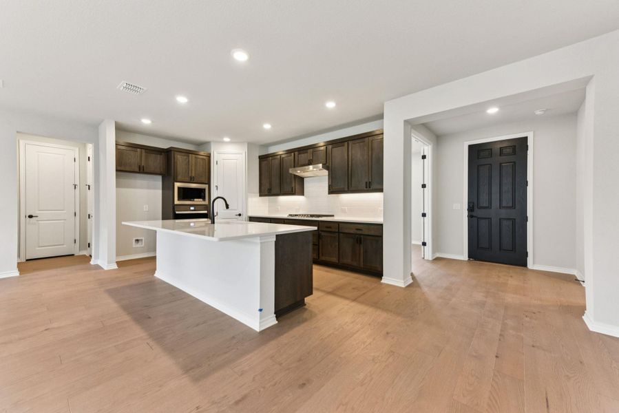 Kitchen featuring recessed lighting, dark brown cabinets, an island with sink, light wood finished floors, and tasteful backsplash