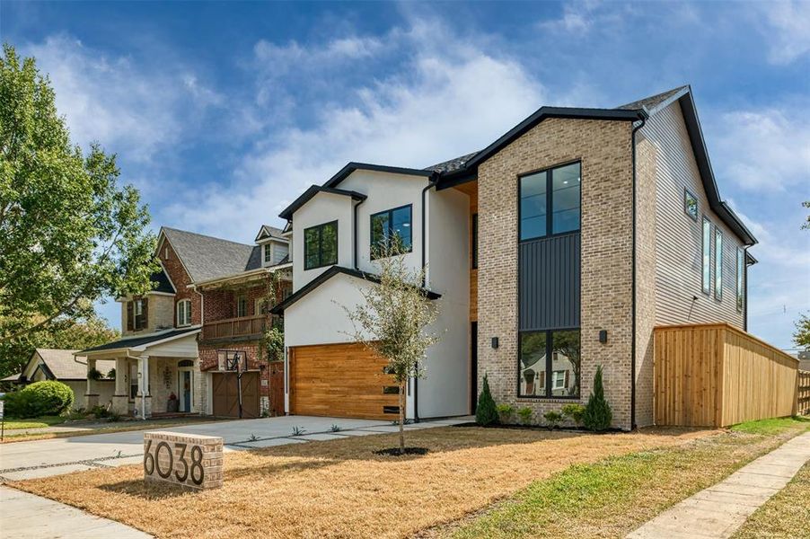 Contemporary house featuring concrete driveway, brick siding, covered porch, a garage, and a front lawn Contemporary house featuring concrete driveway, brick siding, covered porch, a garage, and a front lawn