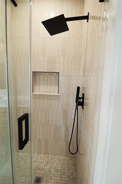 Walk-in shower with rain shower head, matte black fixtures, integrated shelving, vertical picket tile, and pebble-style floor tiling