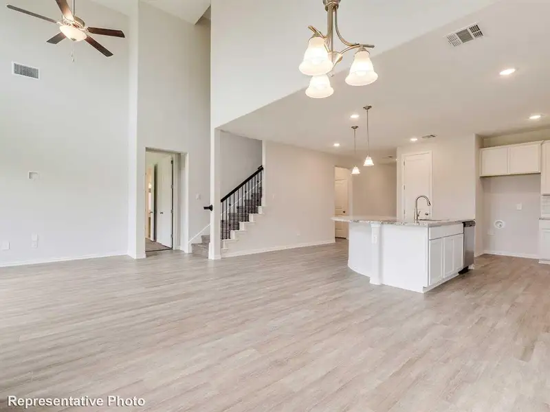 Spacious open-concept interior featuring light-toned flooring, a kitchen island with a sink, and a staircase with dark railings