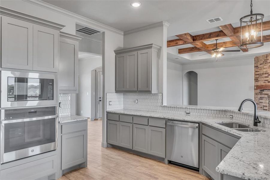 Kitchen featuring light hardwood / wood-style floors, sink, ceiling fan with notable chandelier, coffered ceiling, and stainless steel appliances