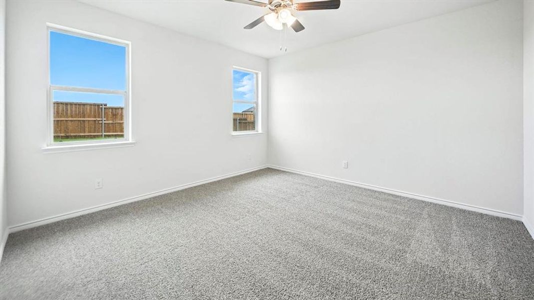 Interior room featuring light gray carpeting, neutral white walls, two windows, and a ceiling fan with integrated lighting